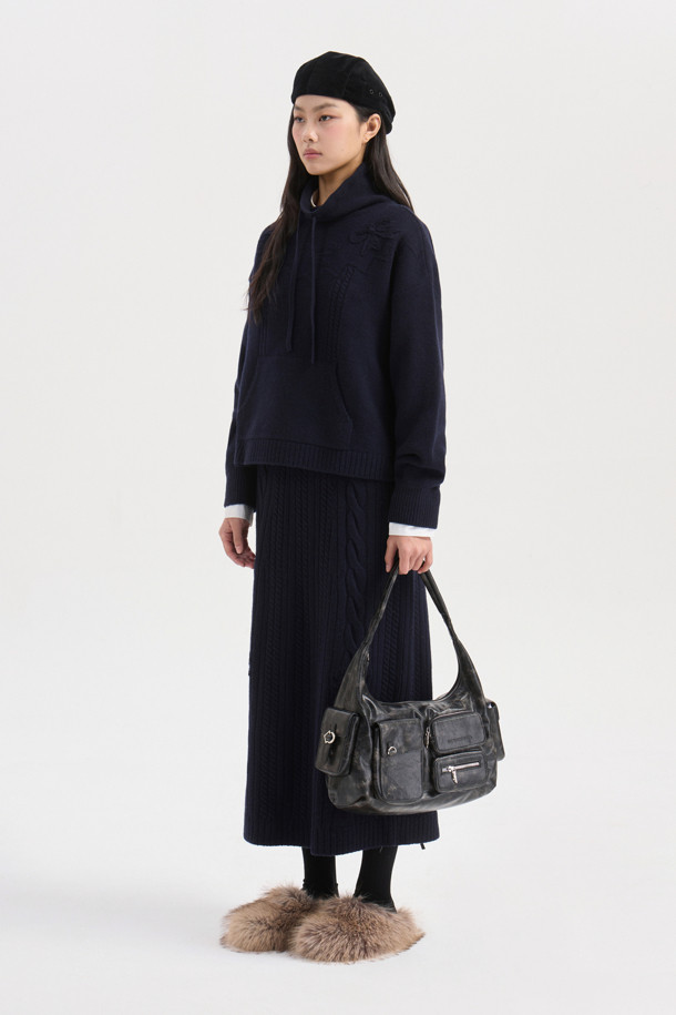 다크 네이비 색상의 리본 니트 스커트입니다. 메리노 울 소재로 제작되어 부드러운 촉감과 따뜻함을 선사하며, 가을/겨울 시즌에 적합합니다. 세미 A라인 핏에 밑단 립조직과 케이블/립조직 패턴이 우아하고 클래식한 분위기를 연출합니다. 허리 부분의 리본 디테일이 여성스러운 포인트를 더하며, 체형 커버에도 효과적입니다. 출근룩과 모임룩 모두 소화 가능한 활용도 높은 맥시 스커트로, 셋업 연출도 가능합니다.
