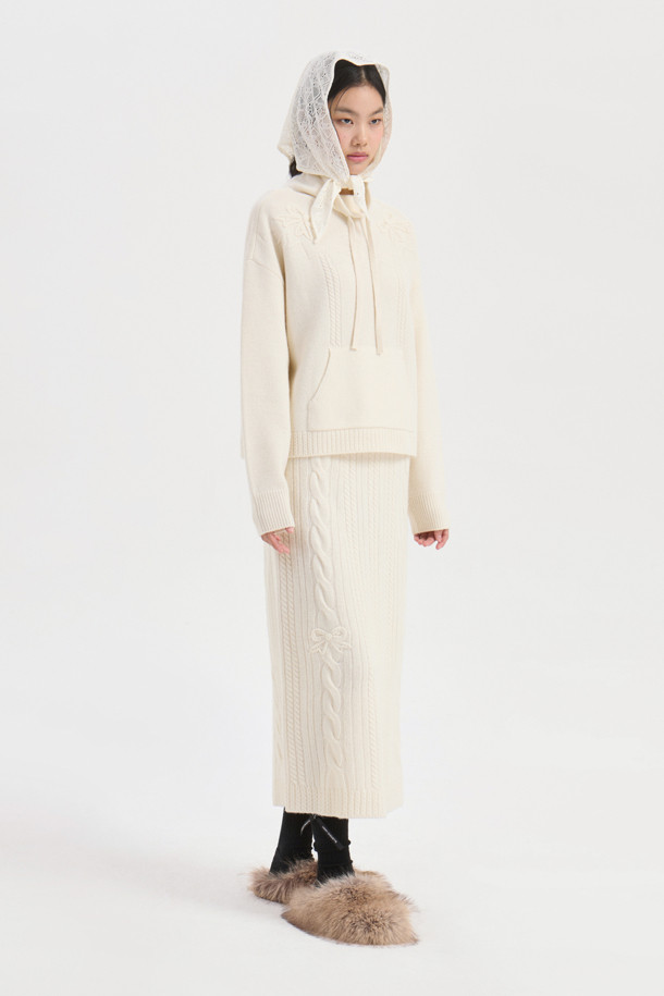 **Ribbon Knit Skirt (아이보리)**

부드러운 메리노울 소재의 리본 니트 스커트입니다. 세미 A라인 핏과 맥시 기장으로 우아한 실루엣을 연출하며, 케이블 및 립조직 패턴이 고급스러운 분위기를 더합니다. 밑단 립조직과 리본 디테일이 돋보이며, 두꺼운 두께감으로 따뜻하게 착용 가능합니다. 가을, 겨울 시즌 데이트룩, 모임룩, 출근룩 등 다양한 TPO에 활용 가능하며, 클래식, 미니멀, 걸리시 스타일을 즐기는 여성분들께 추천합니다. 체형 커버에도 효과적이며 세트업으로도 활용할 수 있습니다.
