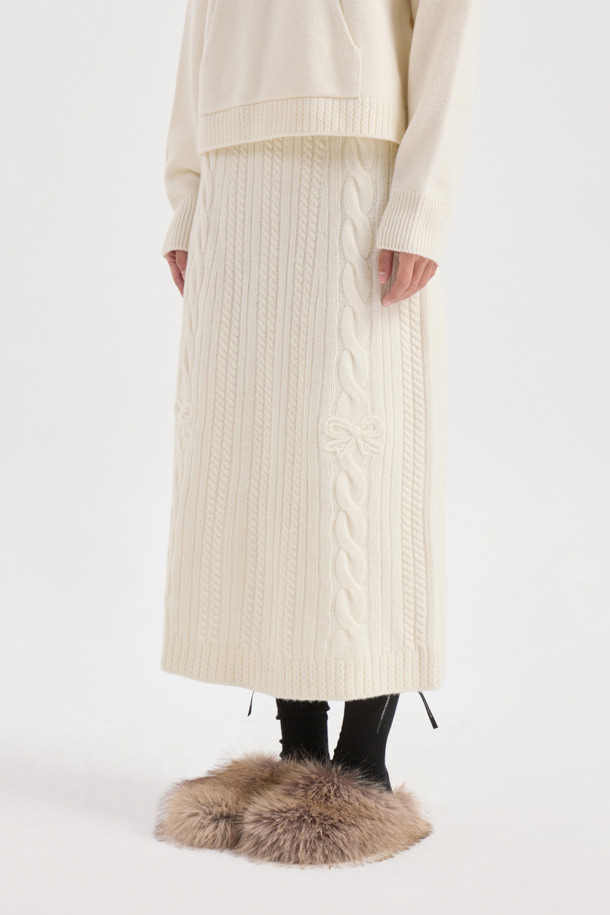 **Ribbon Knit Skirt (아이보리)**

부드러운 메리노울 소재의 리본 니트 스커트입니다. 세미 A라인 핏과 맥시 기장으로 우아한 실루엣을 연출하며, 케이블 및 립조직 패턴이 고급스러운 분위기를 더합니다. 밑단 립조직과 리본 디테일이 돋보이며, 두꺼운 두께감으로 따뜻하게 착용 가능합니다. 가을, 겨울 시즌 데이트룩, 모임룩, 출근룩 등 다양한 TPO에 활용 가능하며, 클래식, 미니멀, 걸리시 스타일을 즐기는 여성분들께 추천합니다. 체형 커버에도 효과적이며 세트업으로도 활용할 수 있습니다.
