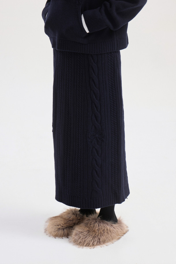 다크 네이비 색상의 리본 니트 스커트입니다. 메리노 울 소재로 제작되어 부드러운 촉감과 따뜻함을 선사하며, 가을/겨울 시즌에 적합합니다. 세미 A라인 핏에 밑단 립조직과 케이블/립조직 패턴이 우아하고 클래식한 분위기를 연출합니다. 허리 부분의 리본 디테일이 여성스러운 포인트를 더하며, 체형 커버에도 효과적입니다. 출근룩과 모임룩 모두 소화 가능한 활용도 높은 맥시 스커트로, 셋업 연출도 가능합니다.

