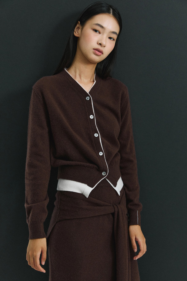 세련된 투톤 배색이 돋보이는 브라운 컬러의 여성 캐시미어 가디건입니다. 몽골산 캐시미어 100% 소재로 제작되어 부드러운 촉감과 뛰어난 보온성을 자랑합니다. V넥 라인과 밑단에 화이트 배색 포인트를 주어 클래식하면서도 세련된 무드를 연출합니다. 레귤러 핏에 얇은 두께감으로 간절기부터 겨울까지 다양하게 활용 가능하며, 버튼 여밈으로 간편하게 착용할 수 있습니다. 데이트룩, 출근룩, 모임룩 등 어떤 TPO에도 잘 어울리는 미니멀 스타일의 가디건입니다.
